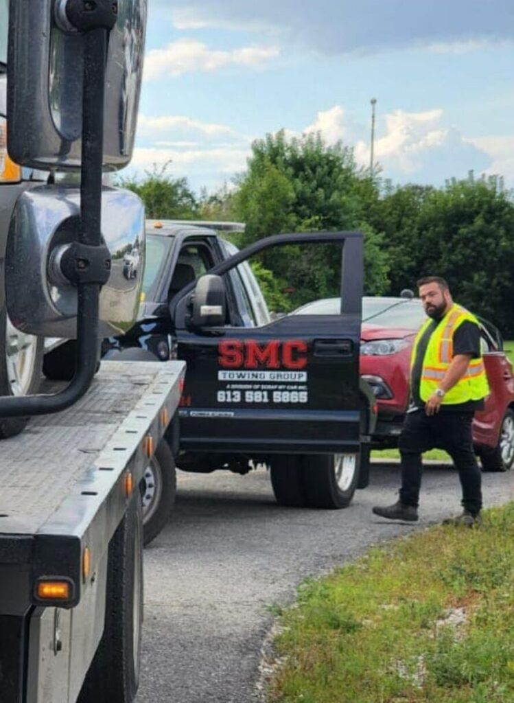 SMC Towing Group operator assisting with a roadside towing service beside a flatbed truck.