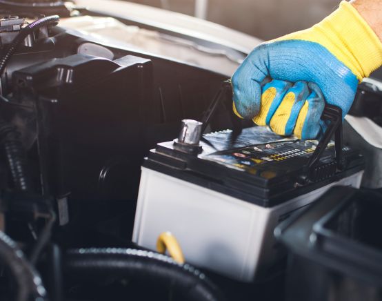 Mechanic wearing gloves installing a new car battery under the hood.