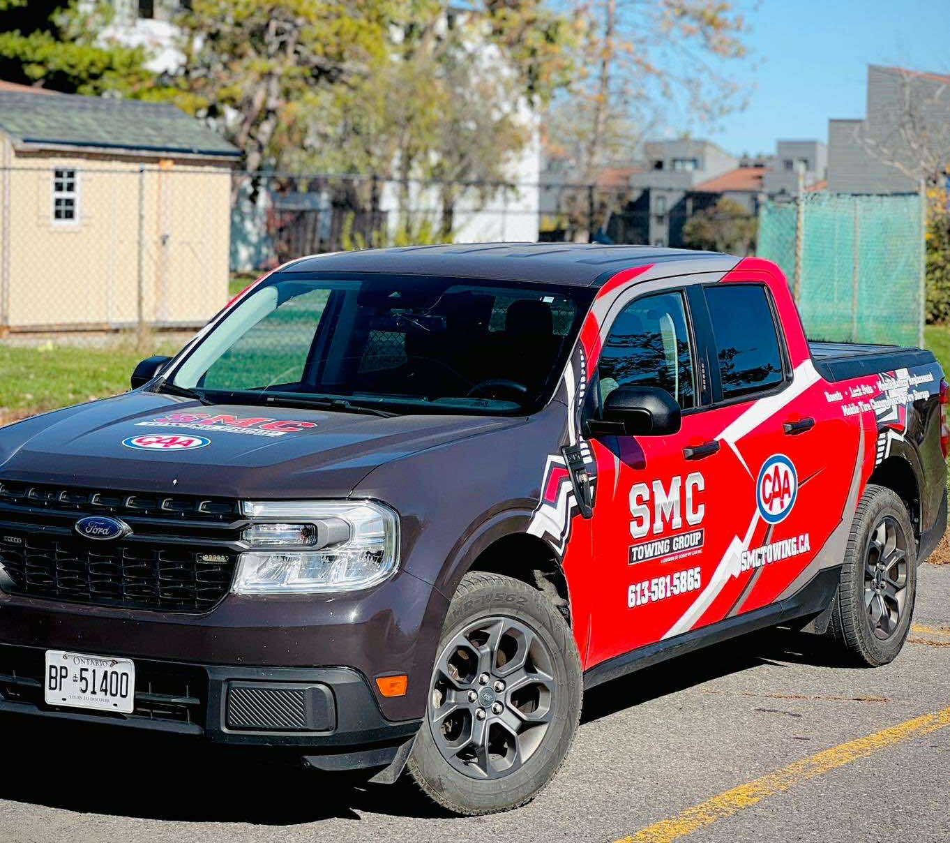 Red and black SMC Towing Group pickup truck with CAA branding parked outdoors on a sunny day.